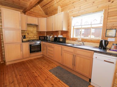 A wooden kitchen with cabinets a stove oven sink dishwasher and small appliances at Sun View Lodge in Llanbedr