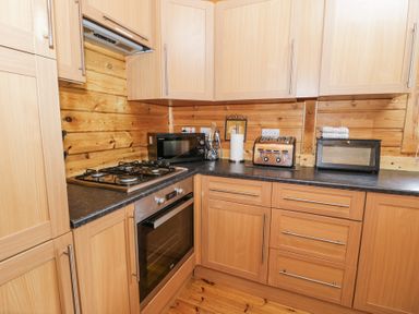 A kitchen with wooden cabinets black countertop microwave gas stove oven toaster and paper towel holder at Sun View Lodge in Llanbedr
