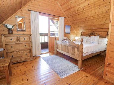 A wooden bedroom with a bed pillows a dresser a mirror and a door leading to a balcony at Sun View Lodge Llanbedr