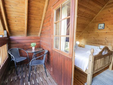 A wooden balcony with two chairs and a small table with a plant next to a bedroom with a wooden bed at Sun View Lodge in Llanbedr