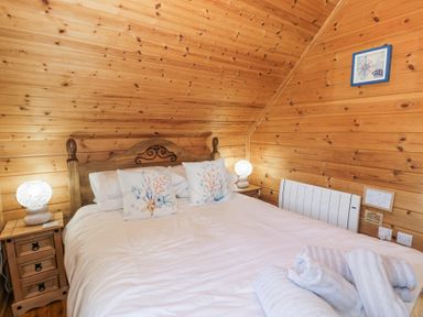 A bedroom with a wooden bed frame white bedding two bedside tables with lamps and wooden walls at Sun View Lodge in Llanbedr