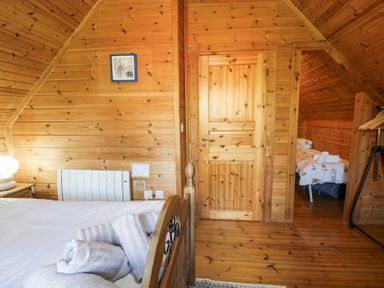 A wooden bedroom with a bed towels a closed door an open door showing another bed and a clothes rack at Sun View Lodge in Llanbedr