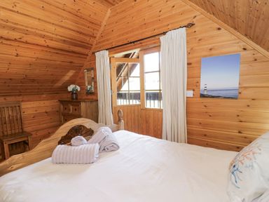 A bedroom with wooden walls a bed with towels a wooden chair a chest of drawers and a window with curtains at Sun View Lodge in Llanbedr