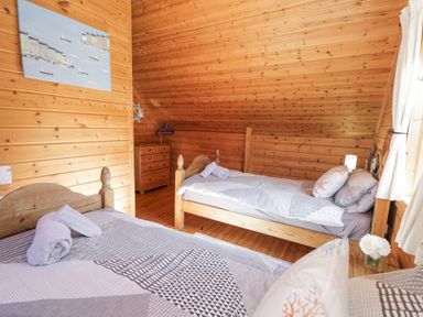 A bedroom with two single beds a wooden chest of drawers and a window with curtains at Sun View Lodge Llanbedr