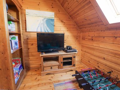 A wooden room with a television and gaming console on a stand a foosball table and a bookshelf at Sun View Lodge in Llanbedr
