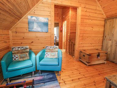A room with two blue armchairs and cushions a wooden chest and a wardrobe at Sun View Lodge Llanbedr