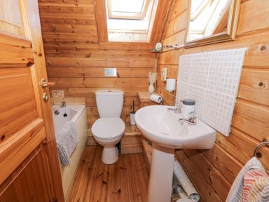 A bathroom with a toilet sink bathtub wooden walls and skylight windows at Sun View Lodge in Llanbedr