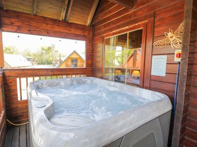 A hot tub on a wooden covered porch with window looking out to other cabins at Sun View Lodge in Llanbedr