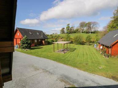 A grassy yard with a wooden pergola and two cabin-style houses with sloped roofs at Sun View Lodge in Llanbedr