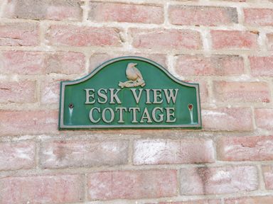 A green sign on a brick wall reading Esk View Cottage at Esk View in Whitby
