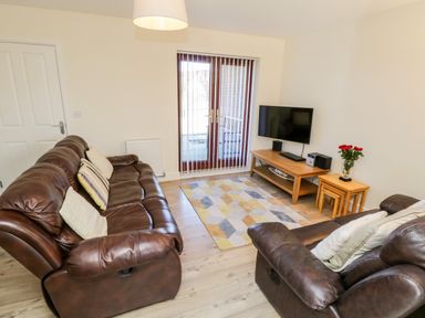 A living room with brown leather sofas a wooden TV stand with a flat screen TV and a side table with flowers at Esk View in Whitby
