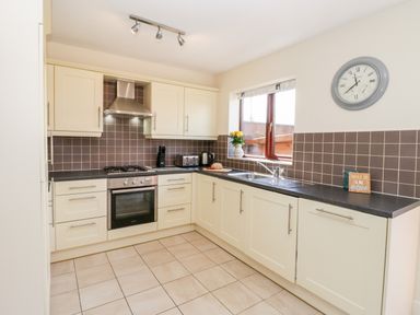 A kitchen with cream cabinets and drawers a black countertop a gas stove an oven a stainless steel extractor fan a window a clock on the wall and flowers on the countertop at Esk View Whitby