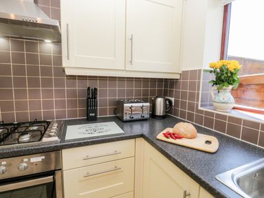 A kitchen corner with a stove oven knife block toaster kettle cutting board with bread and peppers and a vase of yellow flowers on the windowsill at Esk View in Whitby