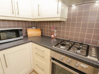 A kitchen corner with a microwave a bread box a bottle of prosecco with two glasses and a gas stove at Esk View in Whitby