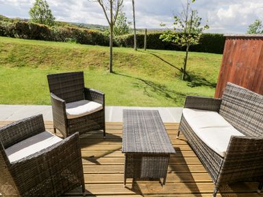 An outdoor patio with wicker furniture consisting of two chairs a loveseat and a table on a wooden deck with a grassy yard and trees in the background at Esk View in Whitby