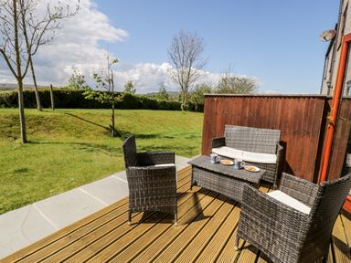 An outdoor deck with wicker chairs a table with mugs and plates next to a grass garden at Esk View in Whitby