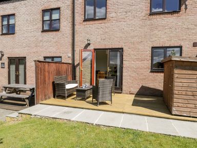 A patio area with wicker furniture and a wooden shed outside a brick house at Esk View in Whitby