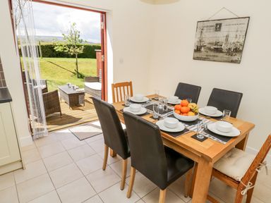 A dining area with a wooden table set with dishes and a bowl of fruit next to open doors leading to an outdoor seating area and garden at Esk View Whitby