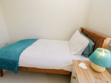A single bed with white and teal bedding next to a wooden nightstand with a teal lamp at Esk View in Whitby