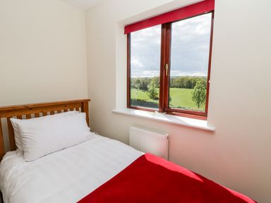 A bedroom with a single bed with white bedding and a red blanket beside a window showing a green landscape at Esk View in Whitby