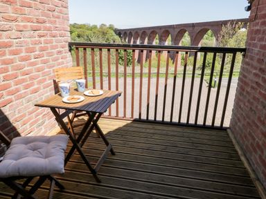 A small balcony with a wooden table and two chairs with cups and plates of biscuits and a view of a brick arched viaduct at Esk View in Whitby