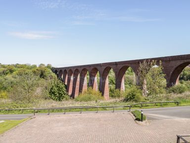 A brick arch bridge over a green wooded valley with a paved parking area and road in the foreground at Esk View in Whitby