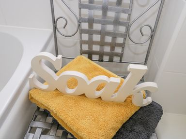 A metal chair with a yellow and a gray towel and a white wooden sign reading soak at Esk View in Whitby