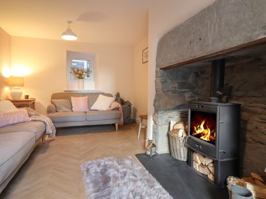 A living room with sofas pillows a small window a lamp and a wood burning stove at Bodlondeb in Tremadog