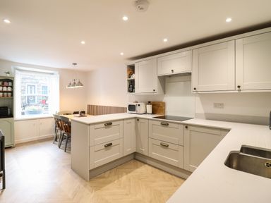 A kitchen with white cabinets countertops a dining table with chairs and a window at Bodlondeb Tremadog