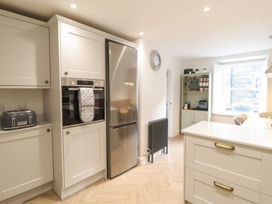 A kitchen with white cabinets a stainless steel fridge an oven a grey toaster and a green shelf with mugs and a coffee machine at Bodlondeb in Tremadog