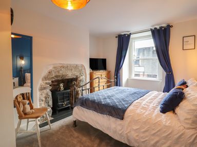 A bedroom with a metal bed frame a wooden chair a stone fireplace and a window with blue curtains at Bodlondeb in Tremadog