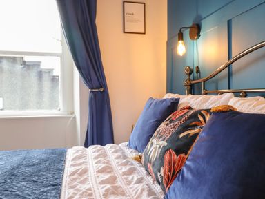 A bedroom with a metal bed frame a white and blue bedspread blue curtains and a wall light at Bodlondeb in Tremadog