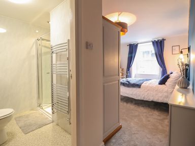 A bathroom with a shower and towel radiator next to a bedroom with a bed blue curtains and a dresser at Bodlondeb in Tremadog