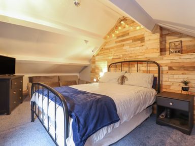 A bedroom with a bed sofa television and wooden wall paneling at Bodlondeb in Tremadog