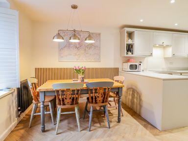 A dining area with a wooden table and colorful chairs next to a white kitchen with cabinets and a microwave at Bodlondeb in Tremadog