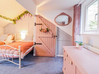 A bedroom with two beds a pink door a pink dresser a mirror and a window at Bodlondeb in Tremadog