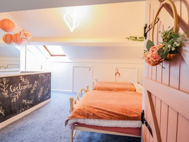 A bedroom with two single beds orange bedding a decorated door and a chalkboard wall with welcome text at Bodlondeb in Tremadog