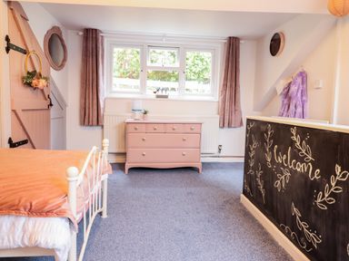 A bedroom with a white metal bed frame orange bedding pink dresser and purple curtains at Bodlondeb in Tremadog
