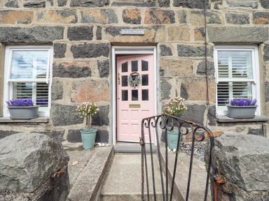 Stone house exterior with a pink door two windows with flower pots and a metal gate at Bodlondeb Tremadog