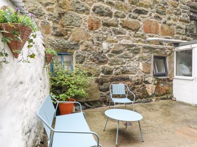 An outdoor patio area with blue metal seating and table stone walls and potted plants at Bodlondeb in Tremadog