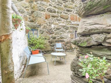 An outdoor stone patio with metal chairs and table with plants hanging on wall at Bodlondeb in Tremadog