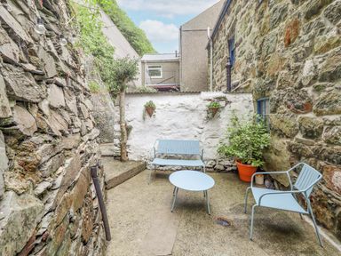An outdoor patio area with stone walls blue metal chairs and table and potted plants at Bodlondeb in Tremadog
