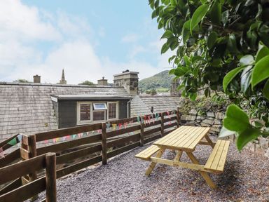 An outdoor seating area with a wooden picnic table and benches next to a wooden fence with colorful bunting at Bodlondeb in Tremadog
