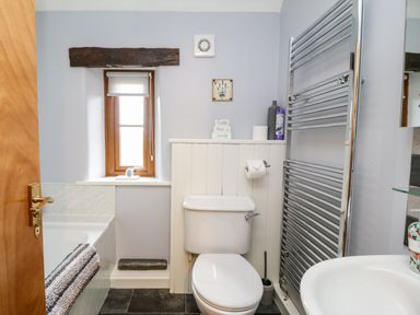 A bathroom with a toilet, sink, towel rack, bathtub, and a window at Lavender Cottage in Penruddock