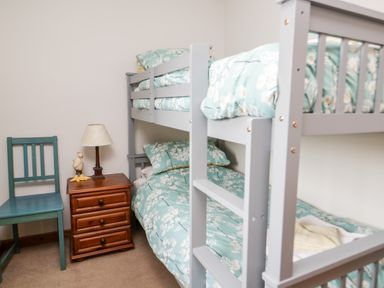 A bedroom with grey bunk beds floral bedding blue chair wooden nightstand lamp and duck figurine at Lavender Cottage in Penruddock
