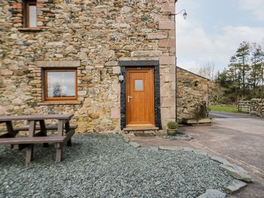 The exterior of a stone building with a wooden door a window a wooden picnic table and a small plant in a pot at Lavender Cottage in Penruddock