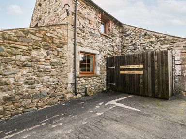 An exterior stone wall with a window and a wooden gate with parking signs at Lavender Cottage in Penruddock