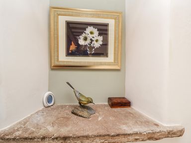 A stone shelf with a bird sculpture a wooden box a small round object and a framed picture of white flowers at Daisy Cottage in Penruddock