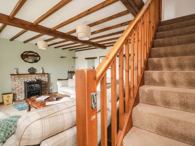A living room with wooden beams on the ceiling a fireplace a wooden coffee table sofas and carpeted stairs at Daisy Cottage in Penruddock