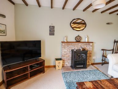 A living room with a television on a wooden stand and a fireplace with a clock and figurines at Daisy Cottage in Penruddock